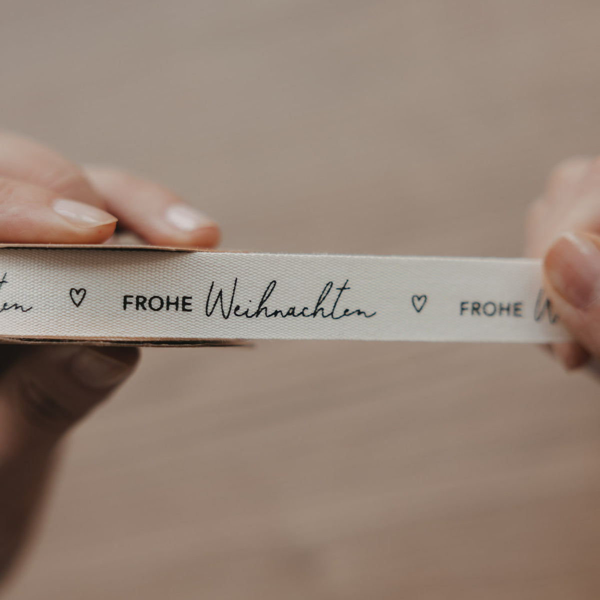 Nahaufnahme: Geschenkband mit „FROHE WEIHNACHTEN“ und Herzsymbolen in Schwarz