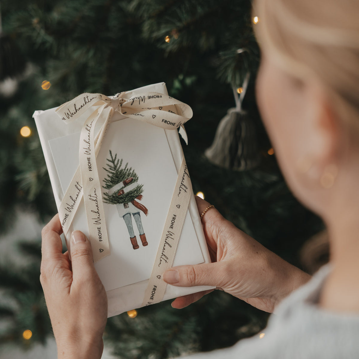 Geschenkband mit Weihnachtsmuster und „FROHE WEIHNACHTEN“ um ein Geschenk gebunden