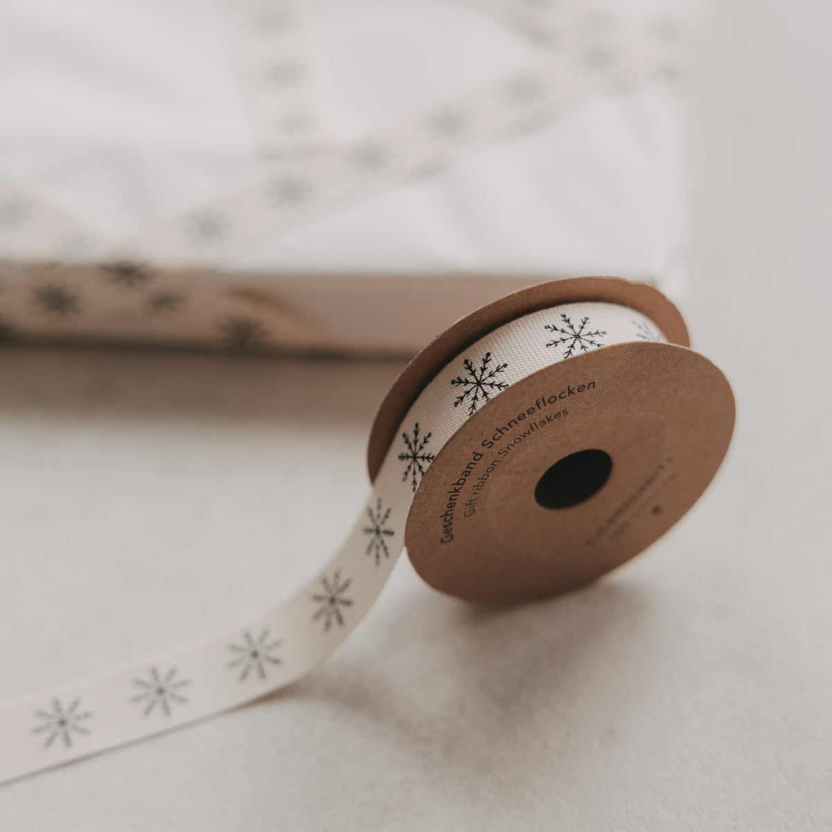 Aufgerolltes beiges Geschenkband mit Schneeflocken-Muster, Etikett auf der Rolle