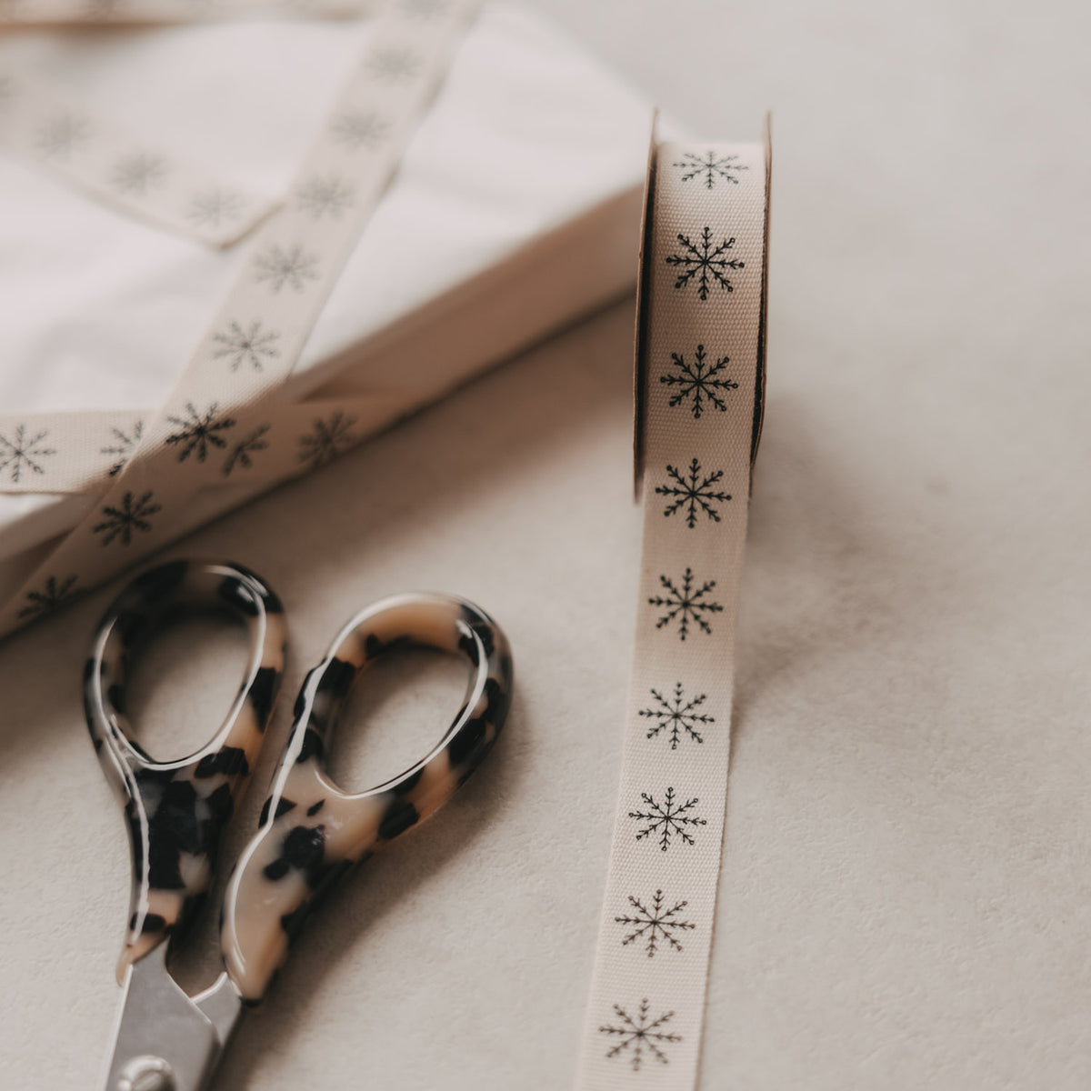 Beiges Geschenkband mit Schneeflocken-Muster, auf Papier abgelegt, Nahansicht