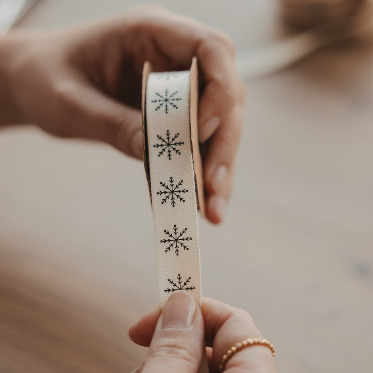 Beiges Geschenkband mit bedruckten Schneeflocken, Bandstreifen in der Hand